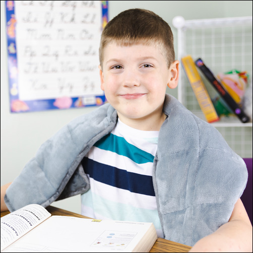 boy sitting at a desk with ta weighted neck wrap around his neck and resting on his shoulders 
