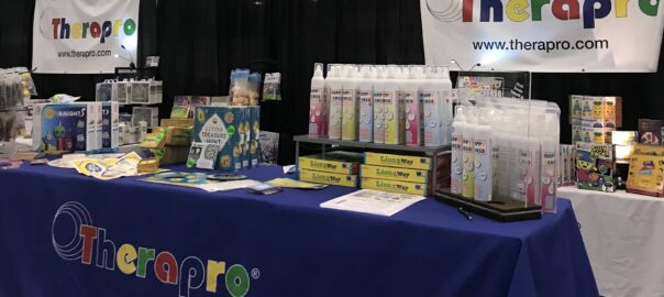 Therapro's Booth at ASHA 2023; table with blue tablecloth and the Therapro logo with Therapro games on display